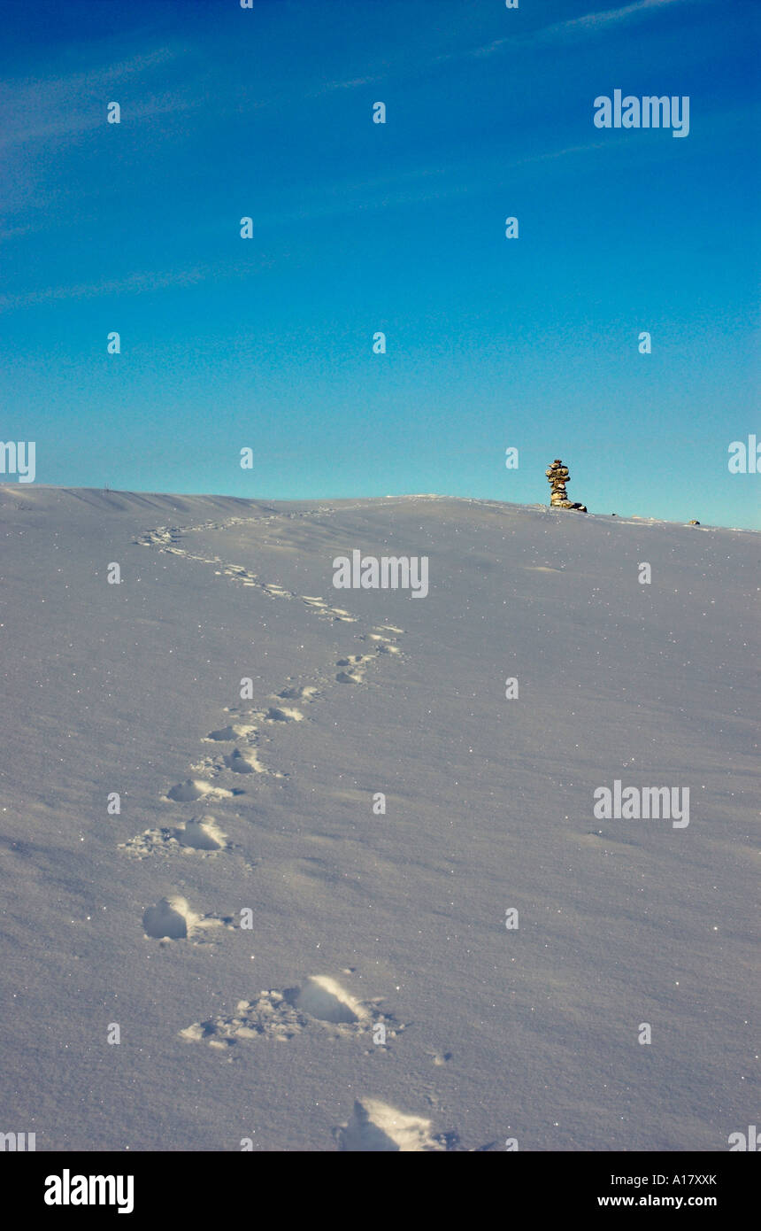 Footsteps in fresh snow leading from an inukshuk on the horizon in the Canadian arctic Stock Photo