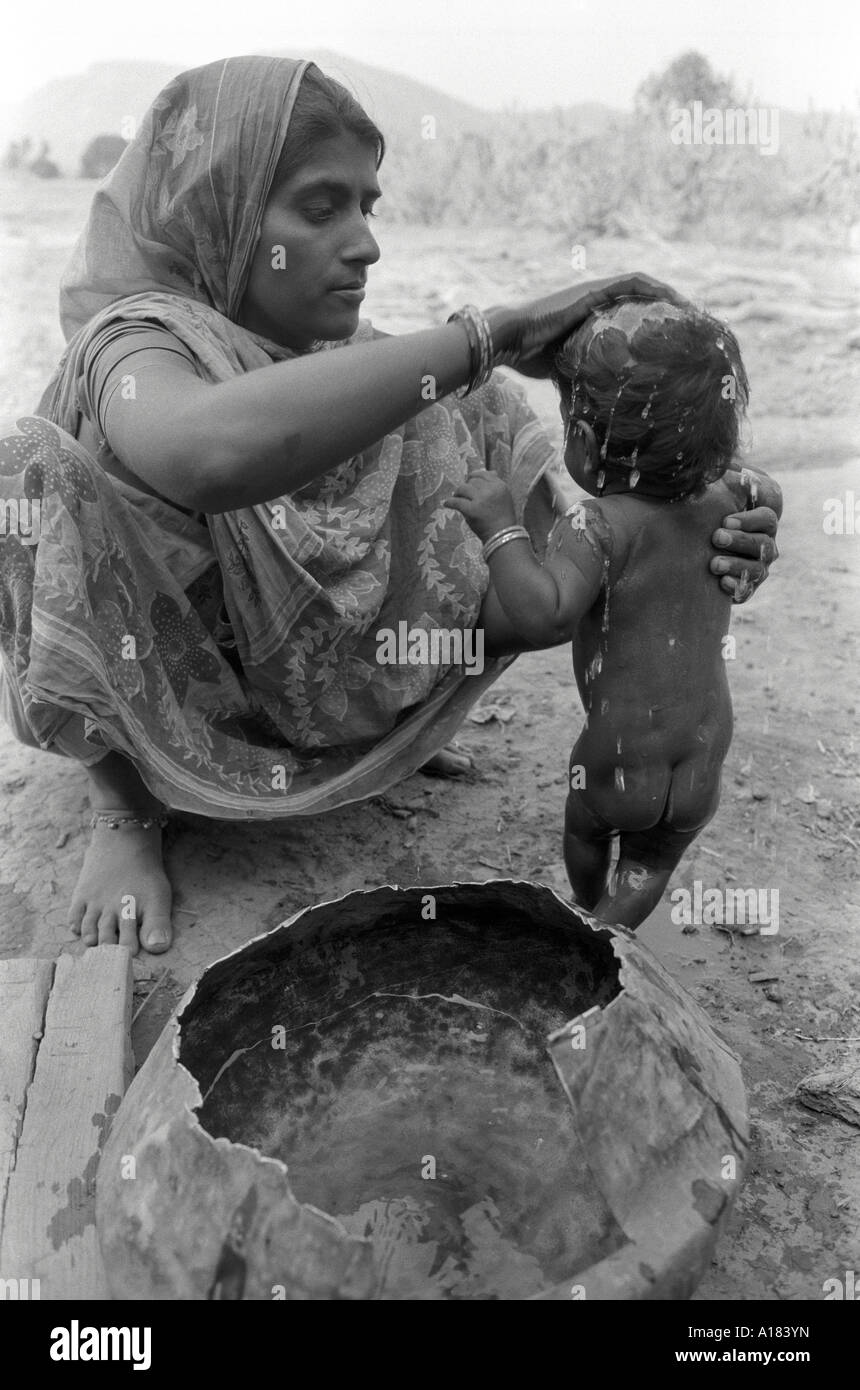 B/W of a female rural farm worker washing her baby from a pot of water. Gujarat, India Stock Photo