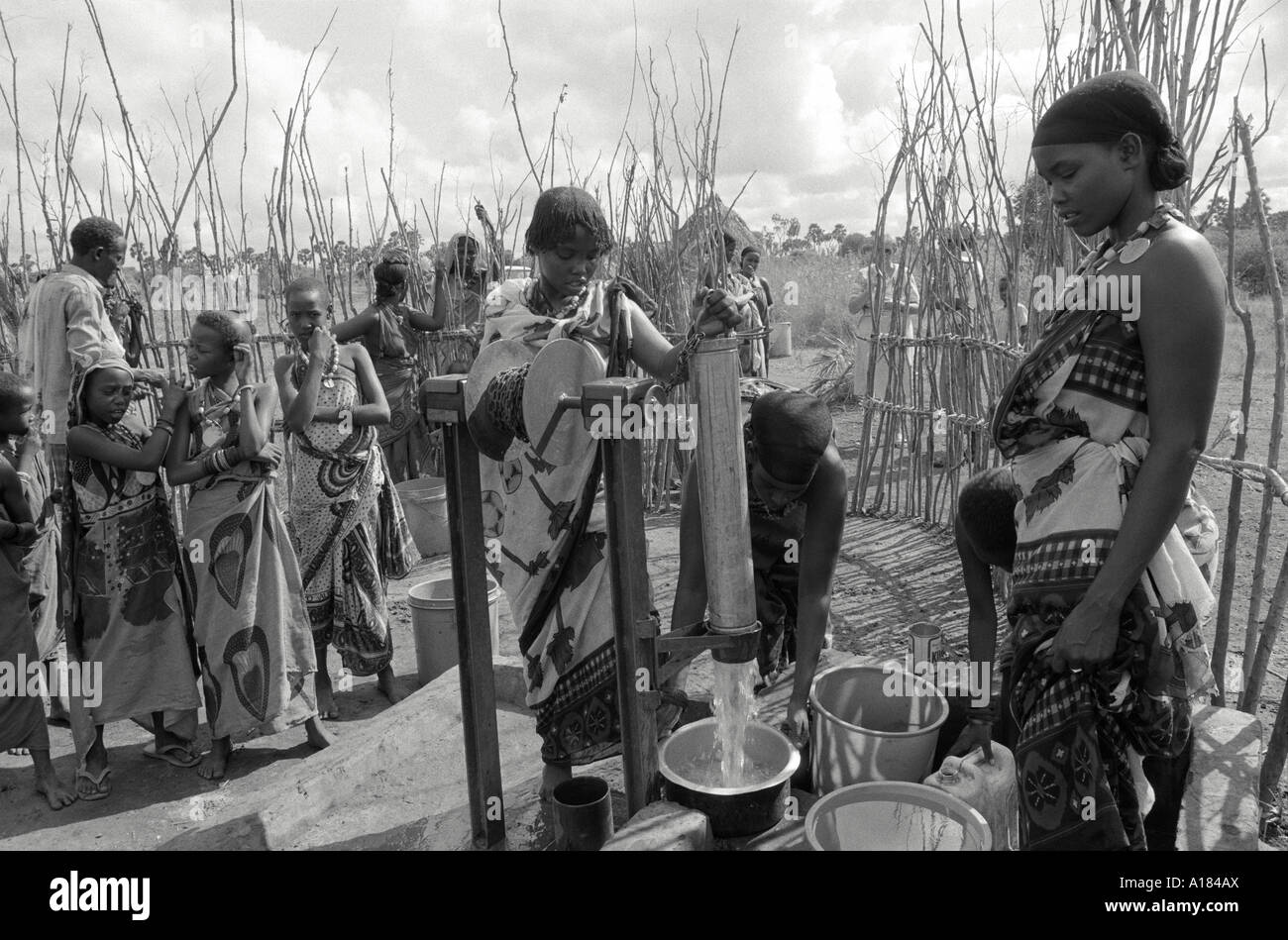B/W of women from the Orma tribe in traditional kangas drawing water from their village water pump in a protected enclosure. Near Wajir, Kenya Stock Photo
