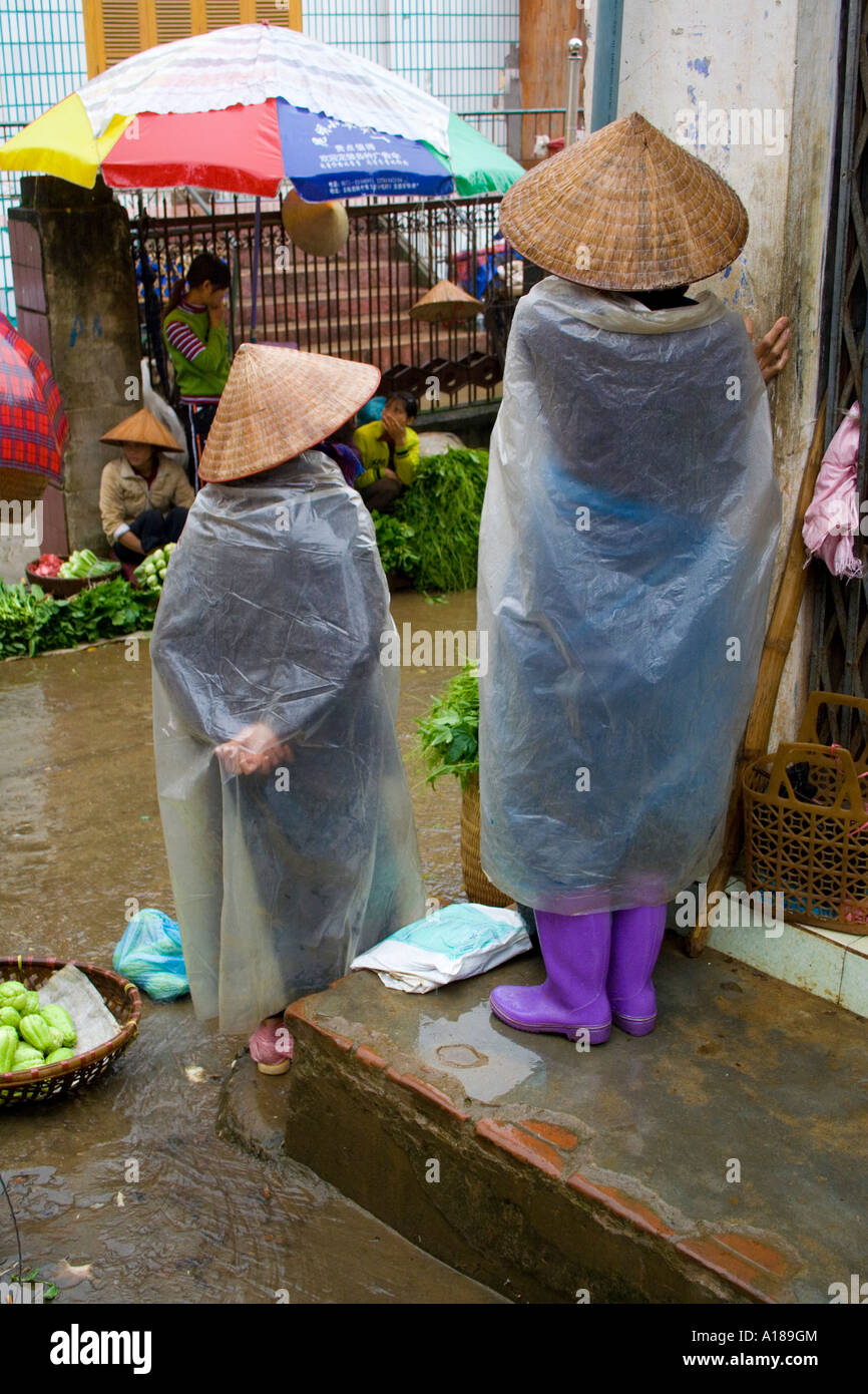 Vietnamese Farmers wearing Traditional Rice Hats and Plastic Rain Covers Sell Fresh Vegetables Sapa Market Vietnam Stock Photo