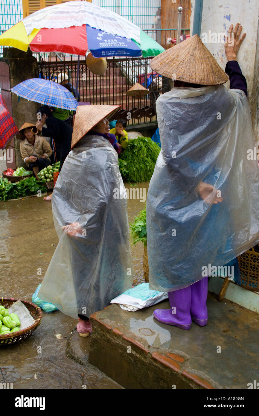 2007 Vietnamese Farmers wearing Traditional Rice Hats and Plastic Rain Covers Sell Fresh Vegetables Sapa Market Vietnam Stock Photo