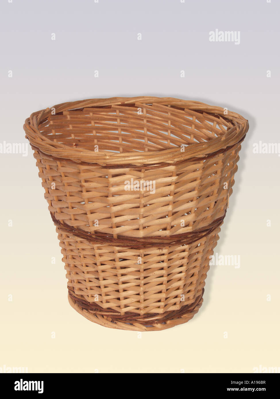 Brown woven wick work cane office waste paper basket on light coloured grey and cream background Stock Photo