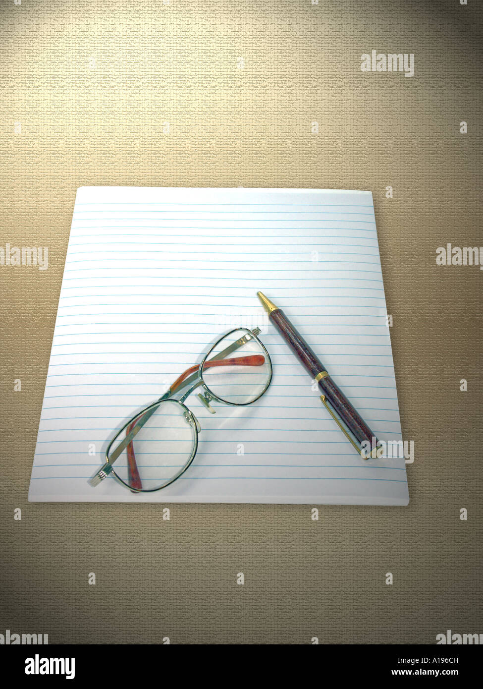 A pad of lined writing paper, reading glasses, and a ballpoint pen on a light patterned fabric background Stock Photo