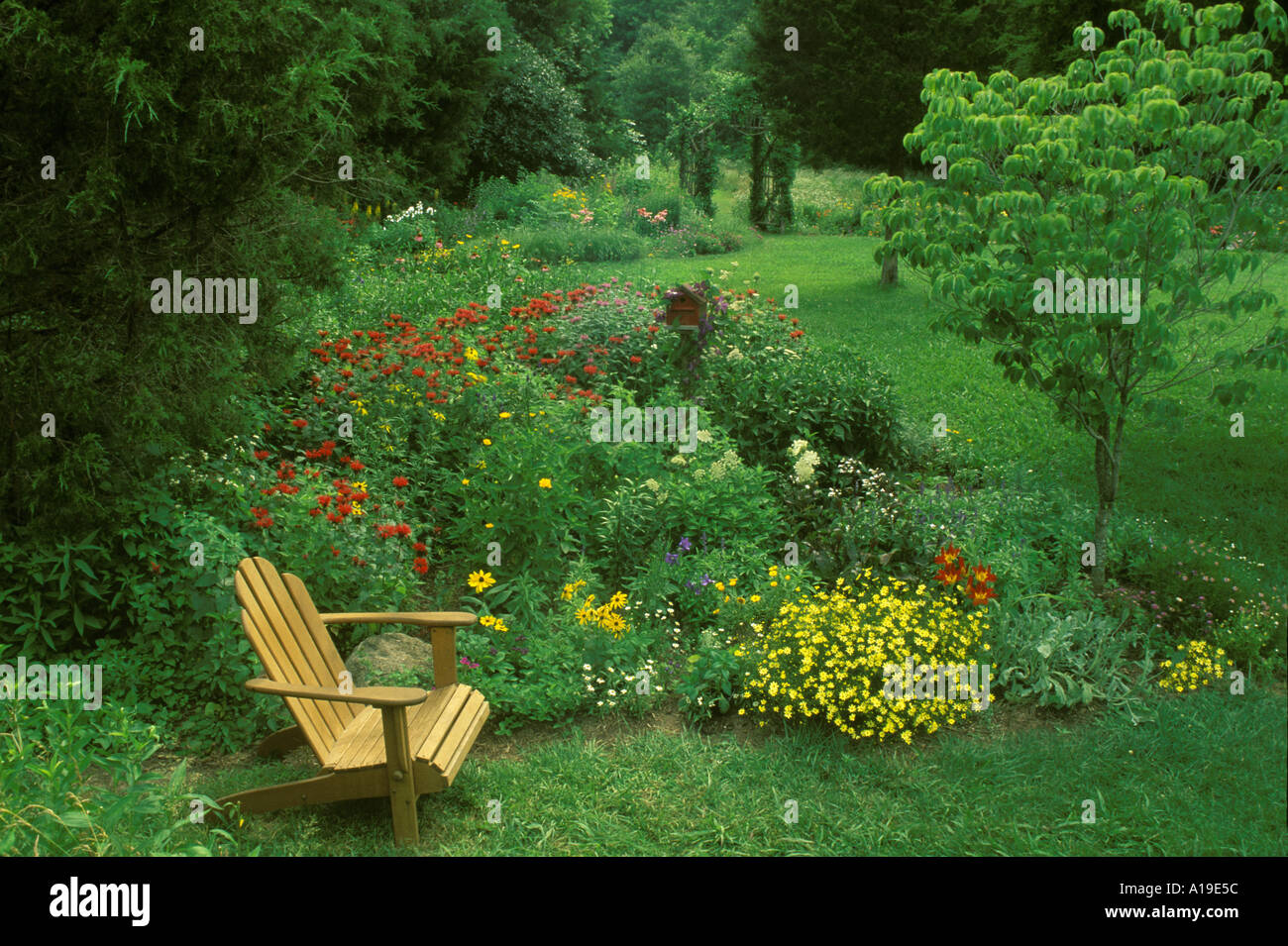 Adirondack chair in large home blooming flower garden with birdbox and cedar arbor, Missouri USA Stock Photo