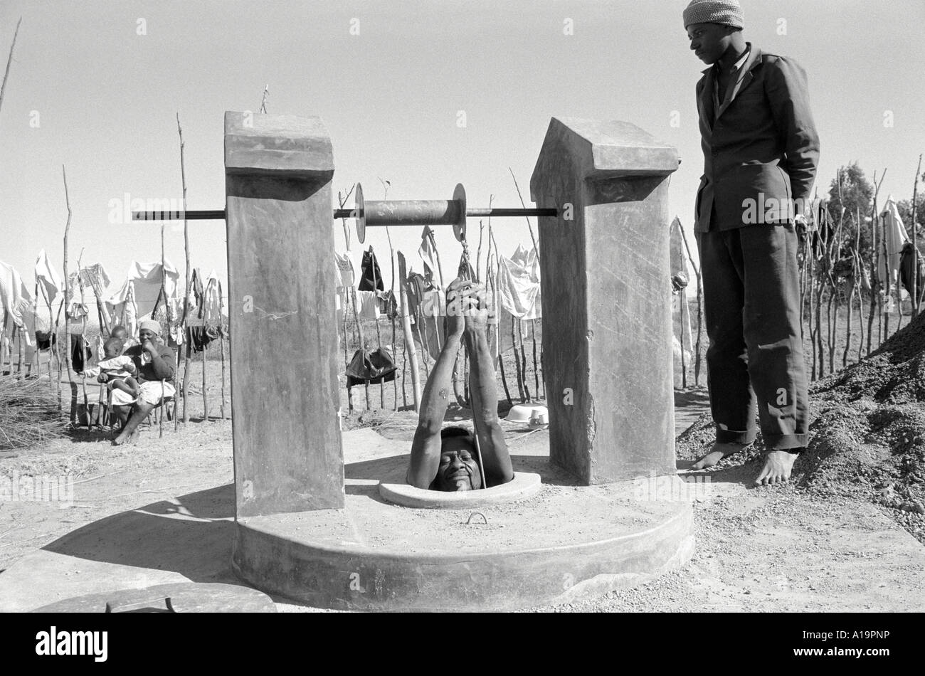 B/W of a man being lowered into a water well to deepen it during a long period of drought. Nr. Kwekwe, Zimbabwe Stock Photo