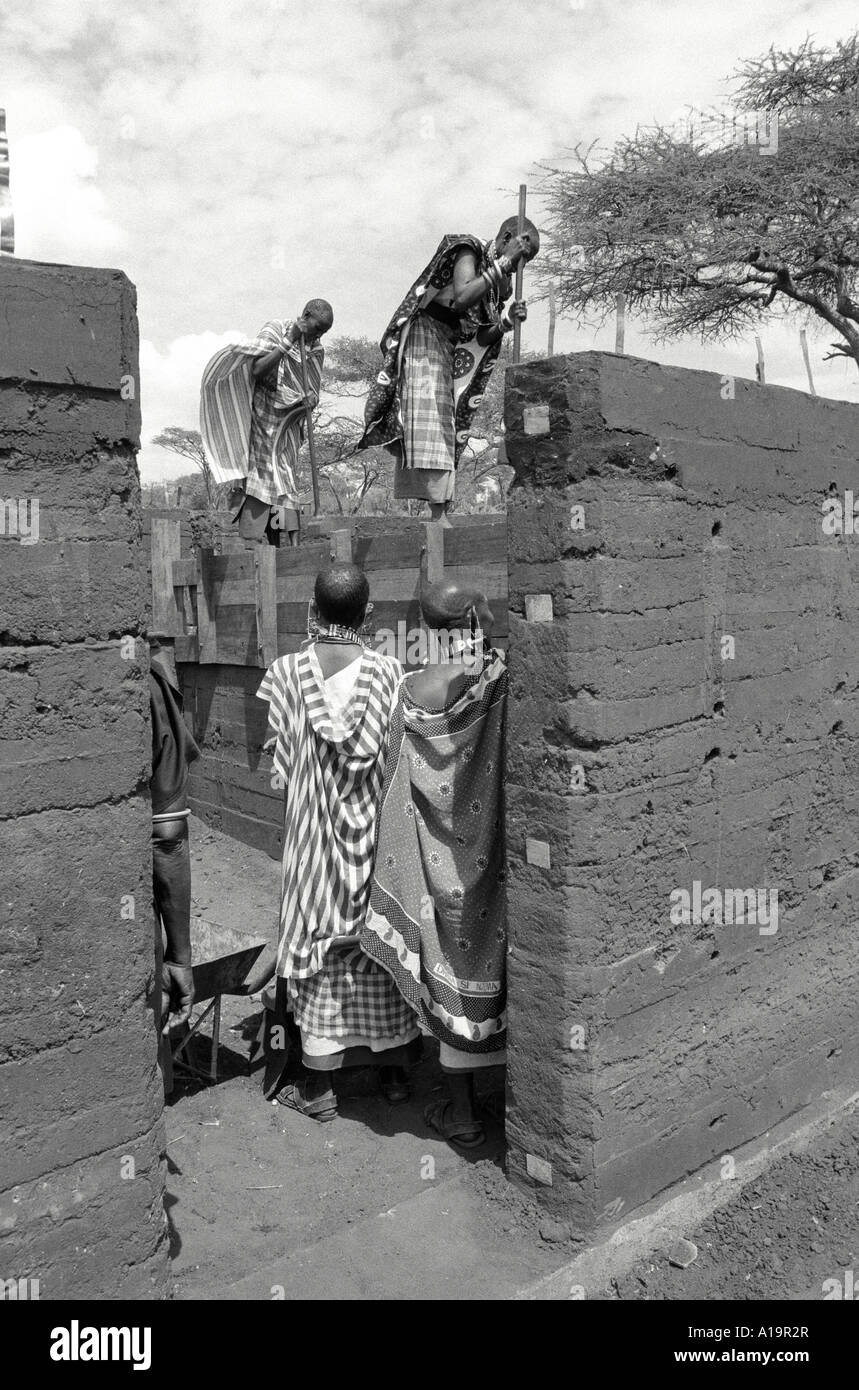 B/W of Maasai women in traditional dress building rammed earth, longer lasting housing in their community. Kajiado, Kenya Stock Photo