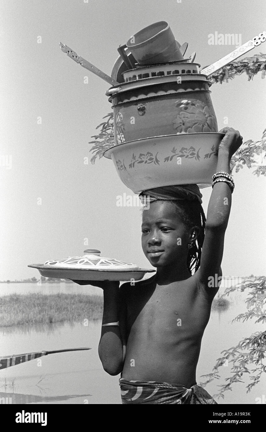 B/W of a young girl from the Bozo tribe balancing kitchen pots and pans ...