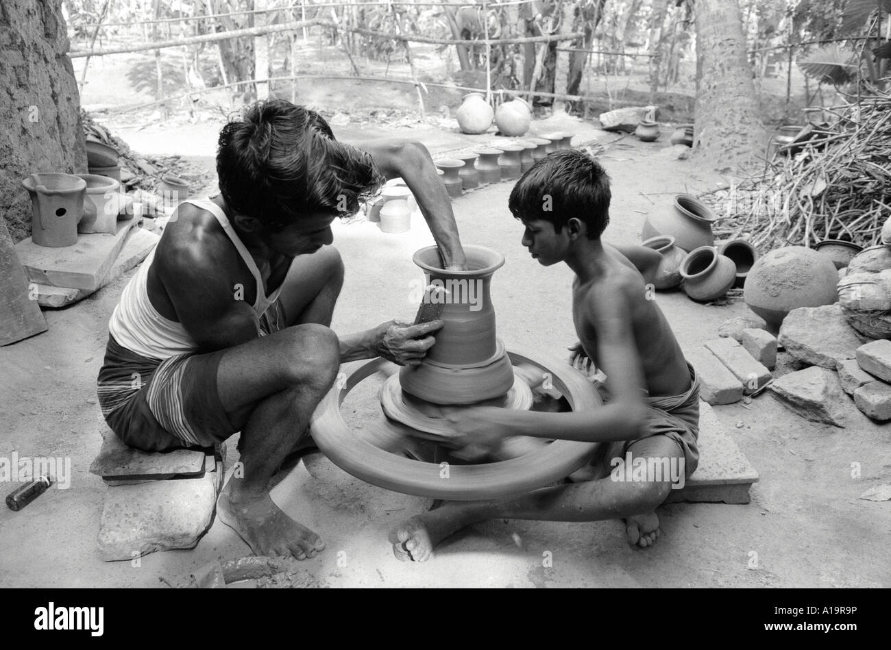 B/W of a young boy turning a potter's wheel for his father who is making a clay pot, a low-caste occupation in Tamil Nadu, South India Stock Photo