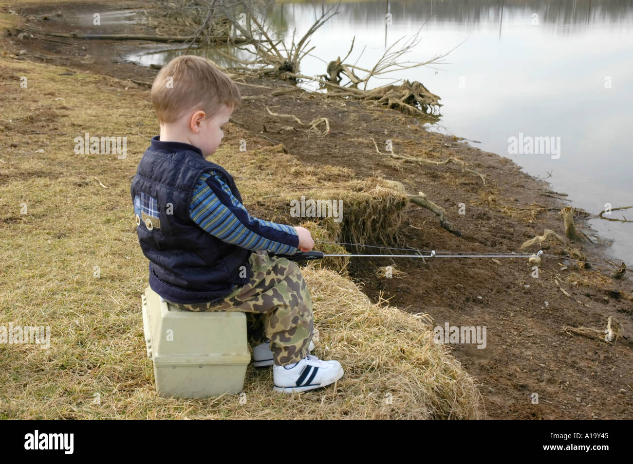boy fishig with tackle box Young boy sitting on a tackle box while fishing Stock Photo