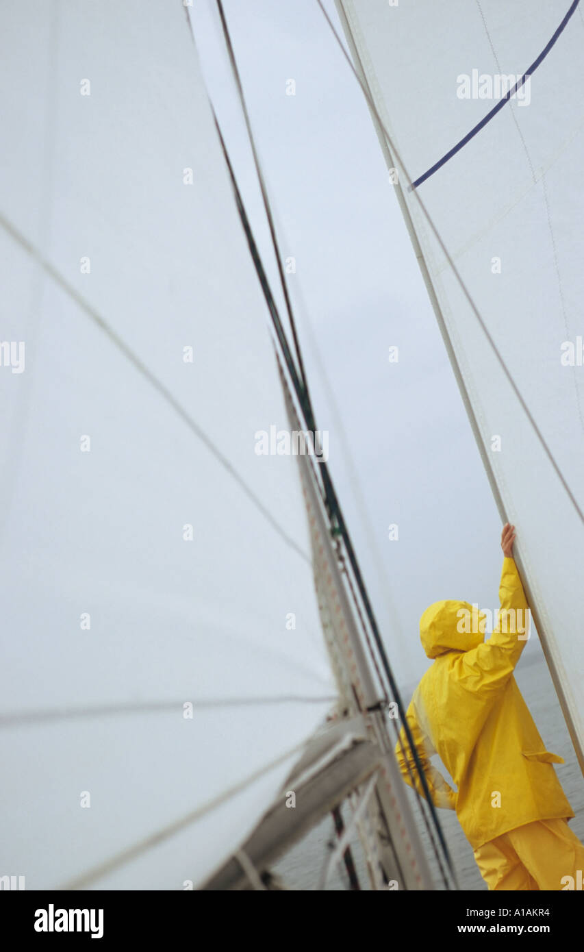 Person on boat in yellow waterproofs leaning on sail Stock Photo