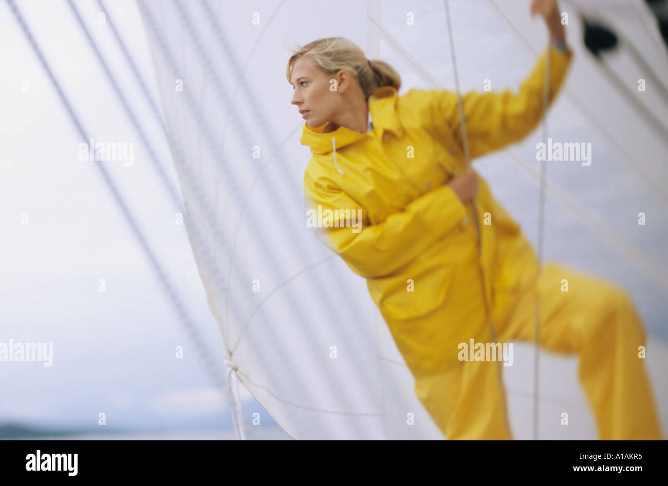 Woman on boat in yellow waterproofs holding rope Stock Photo