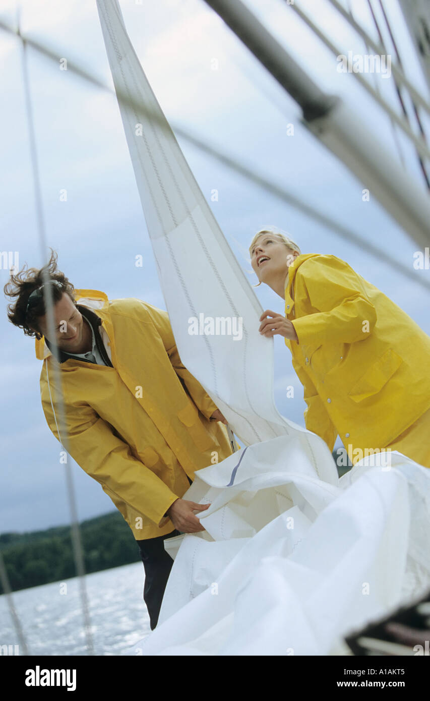 Couple taking down sail on boat Stock Photo