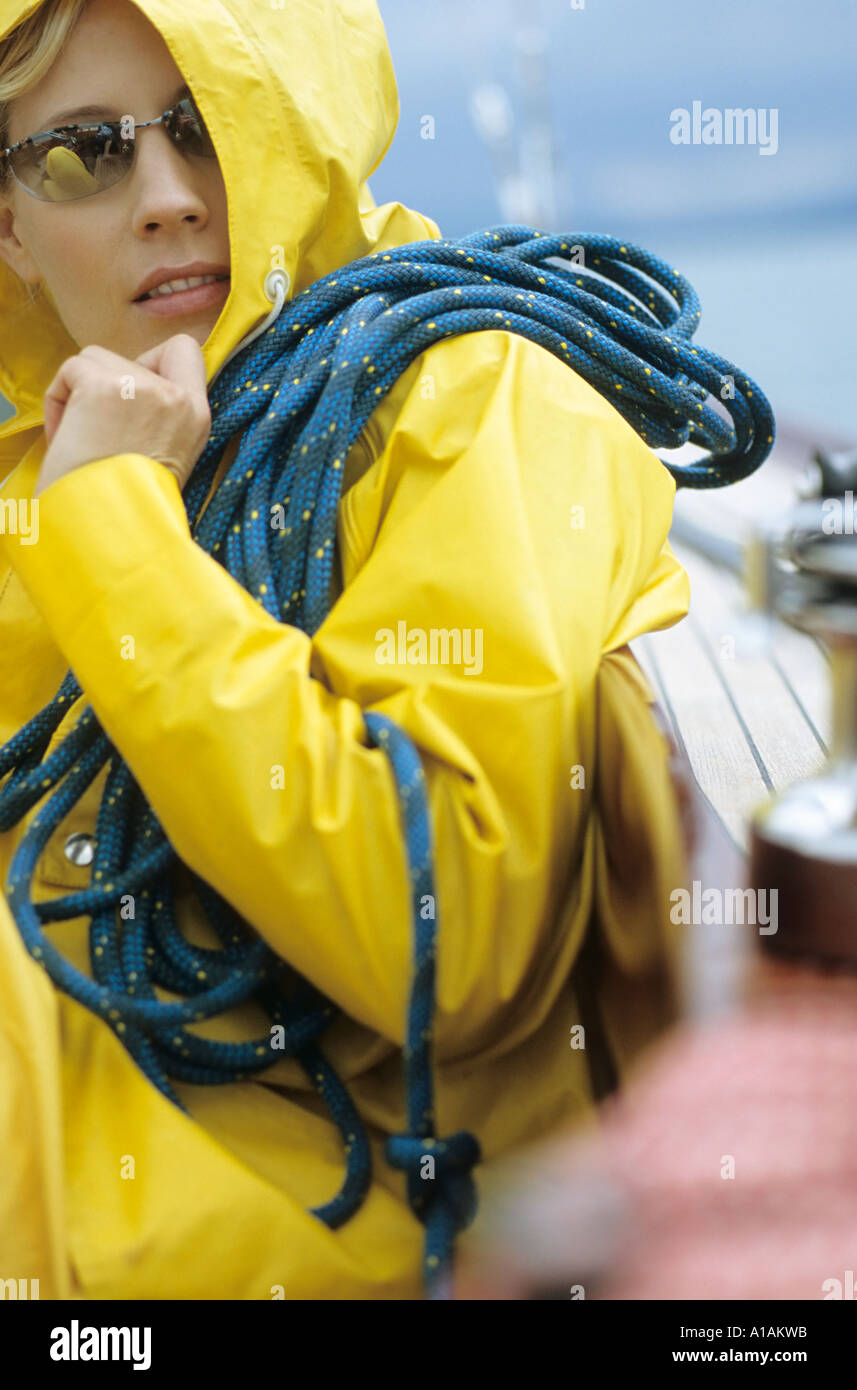 Woman in yellow raincoat and sunglasses carrying rope Stock Photo