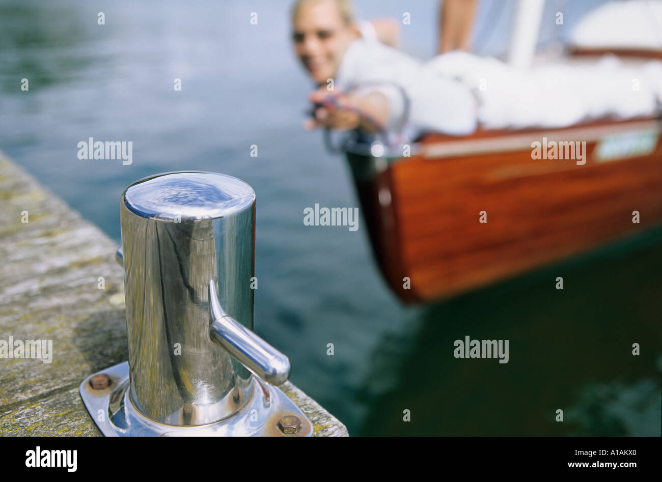 Woman on boat reaching out towards bollard on jetty Stock Photo