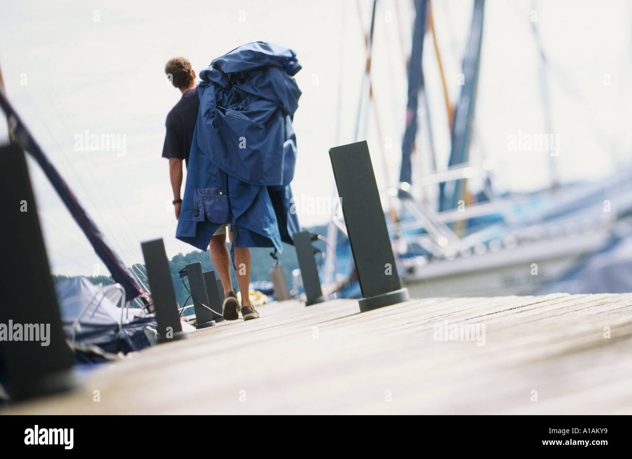 Man walking along jetty carrying boat cover Stock Photo