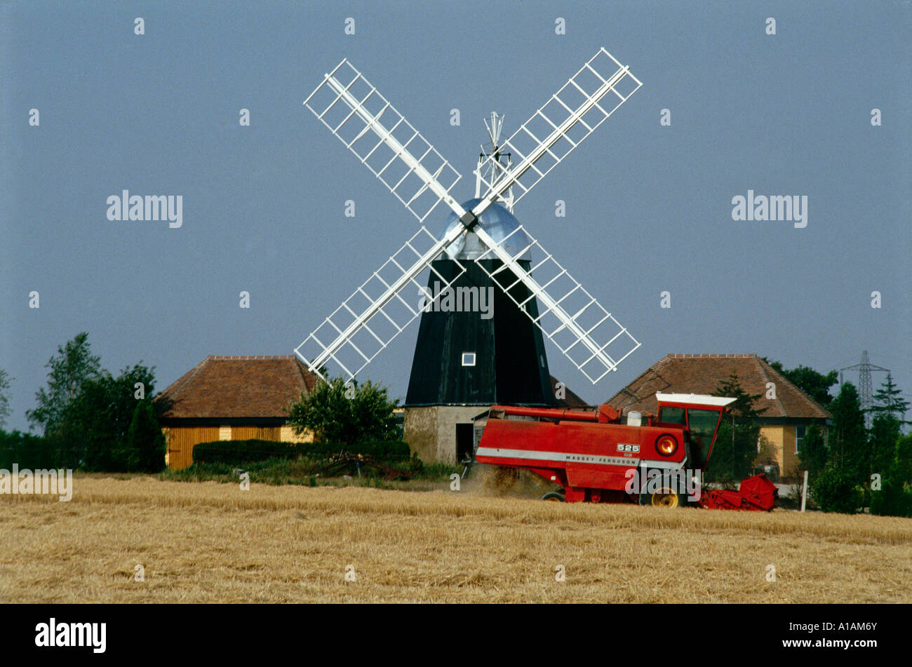 19th century Smock Tower Mill from across a field with a combine harvester in front of it Swaffham Prior Stock Photo