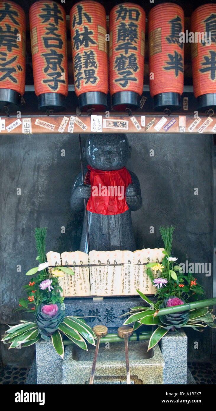 Stone carved Jizo statue in a red bib underneath a row of paper lanterns at a temple in central