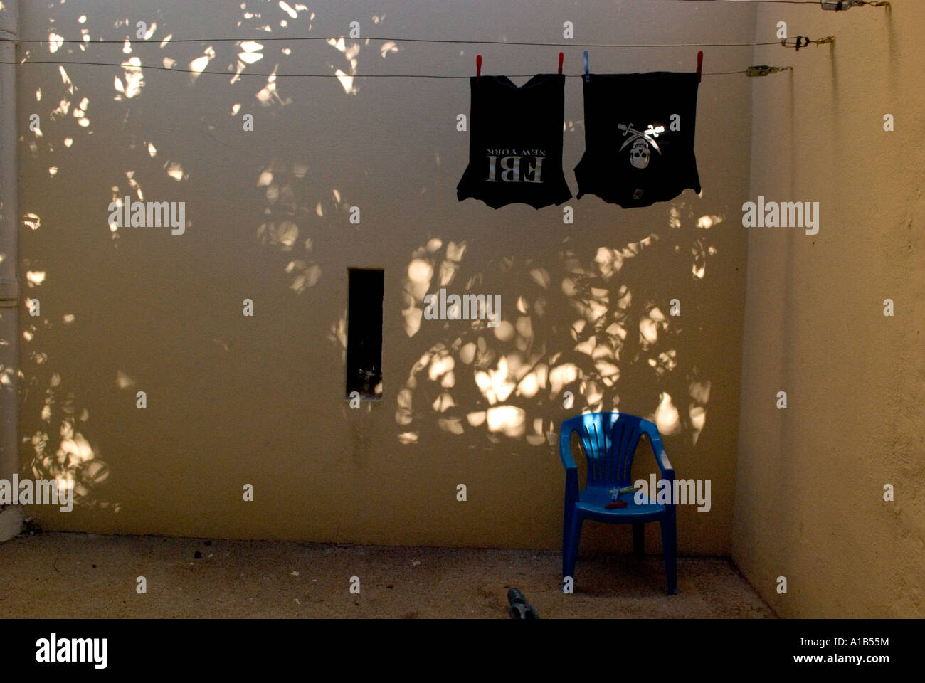 two kids t-shirts hanging to dry on a washing line above a small blue plastic chair Stock Photo