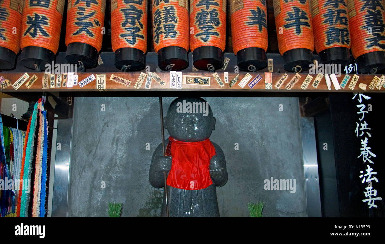 Stone carved Jizo statue in a red bib underneath a row of paper lanterns at a temple in central