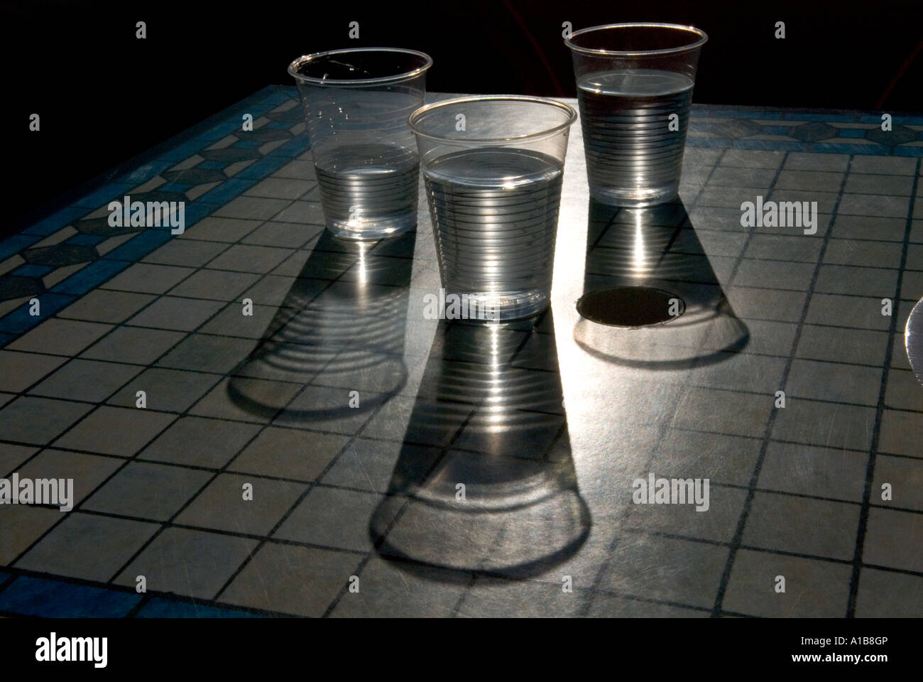 three transparent plastic cups of water with long shadows on a cafe