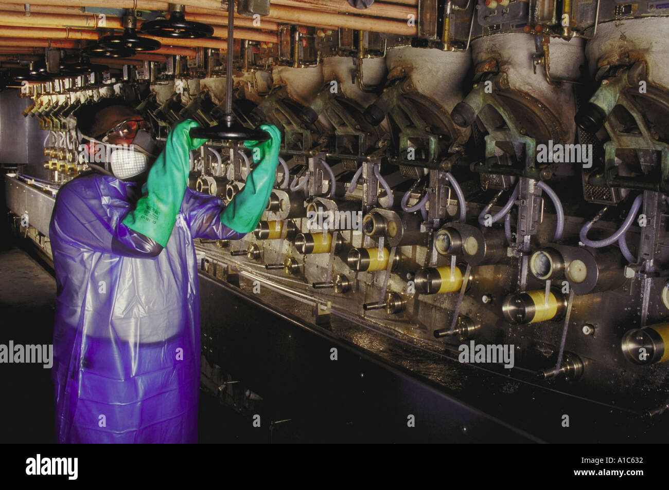 Production Machine Operator dressed in plastic gown rubber gloves safety glasses and respirator Stock Photo