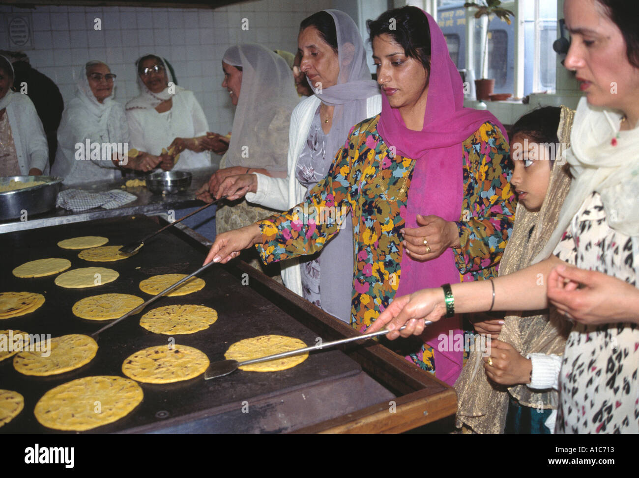 A cook in a Sikh kitchen cooking in an extremely large pot.