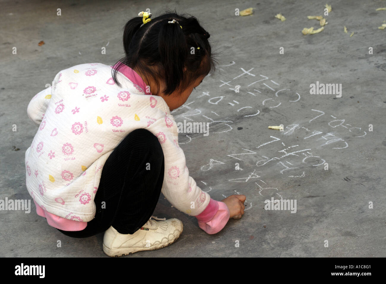 Little girl practices math with chalk on the concrete at the antique market in zhongshan, China Stock Photo