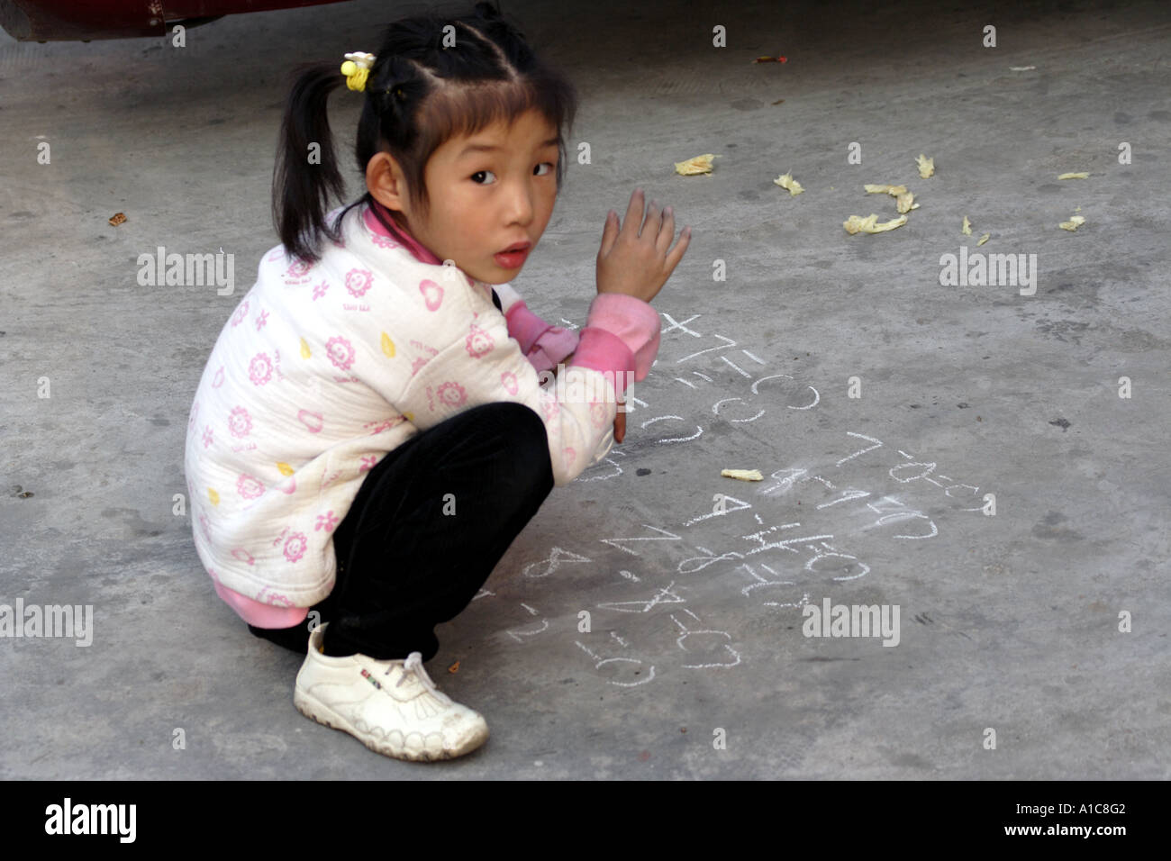 Little girl practices math with chalk on the concrete  Zhongshan, China Stock Photo