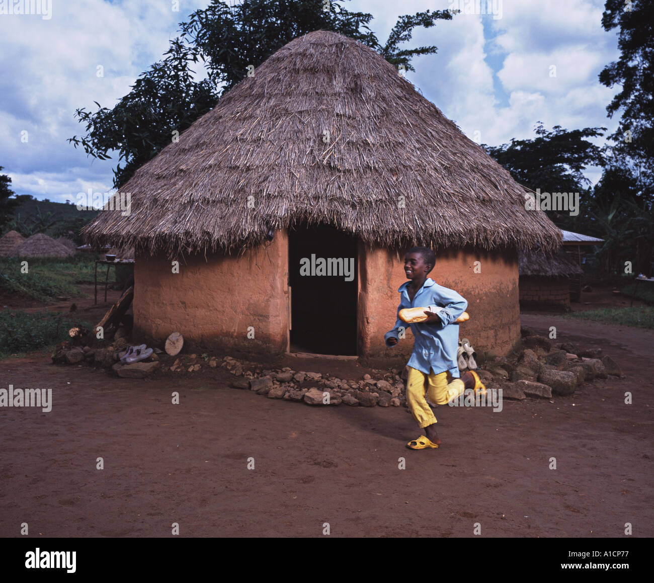 Young boy running past mud hut with bread Stock Photo