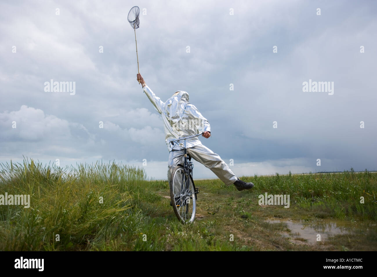 Man in firefighter costume stretching to catch butterflies riding a bicycle in a marshland Stock Photo