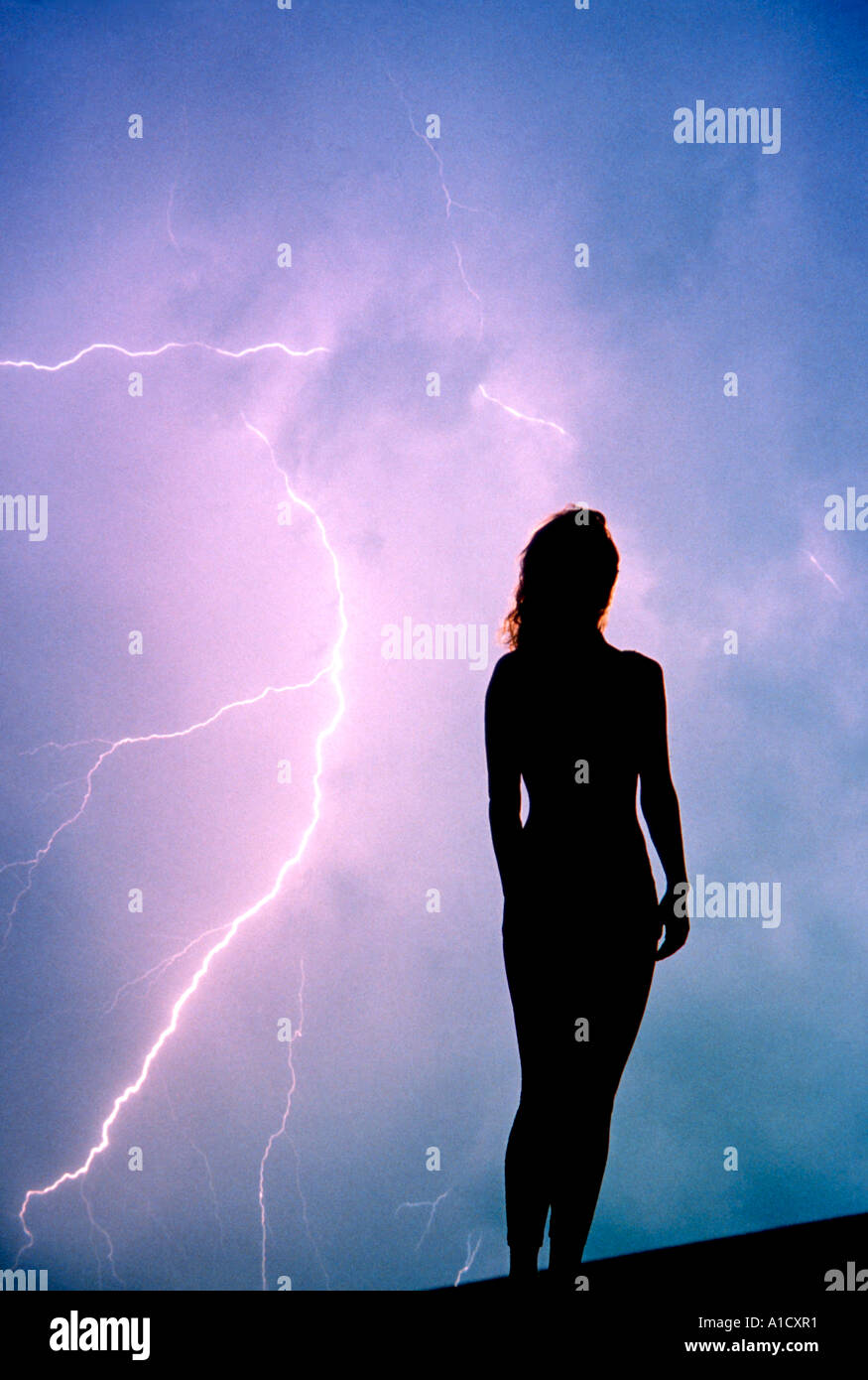 silhouette of woman with lightning and storm clouds in background Stock