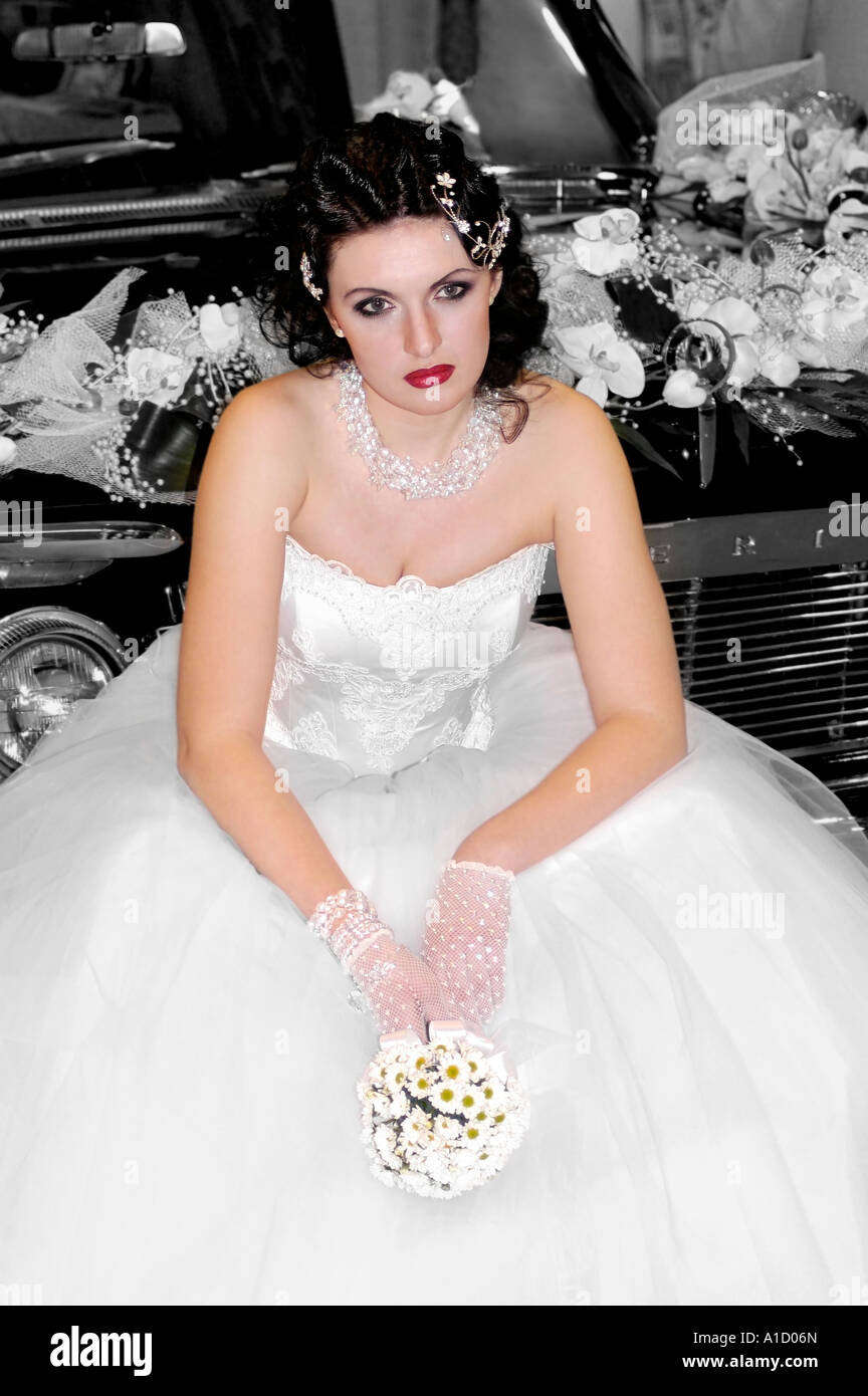 Lonely Bride Young woman in wedding gown siting on a car Stock Photo