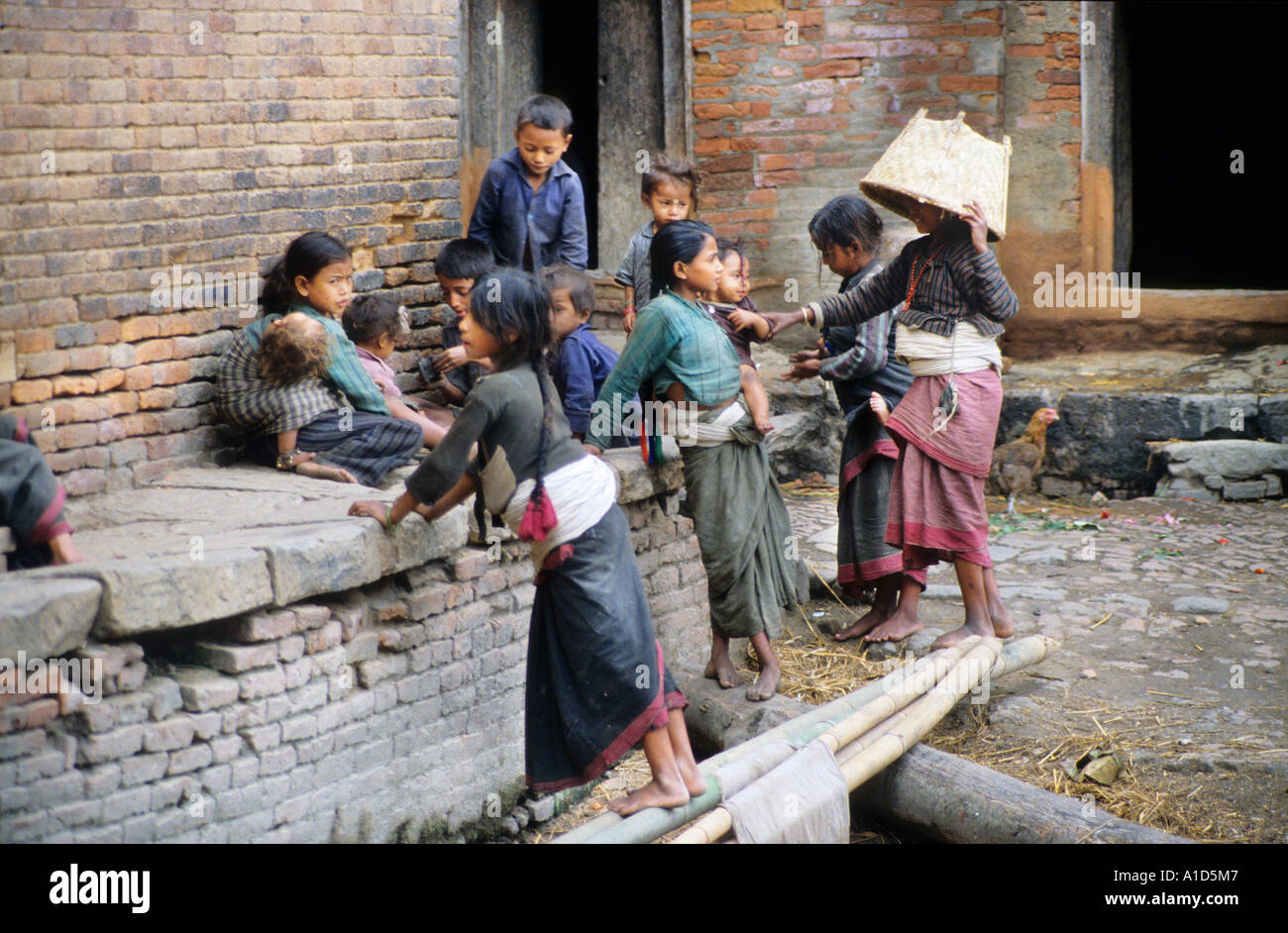 Group of young people in courtyard boy girl bare feet basket bricks ledge sit sat talk communicate house home door doorway rest Stock Photo