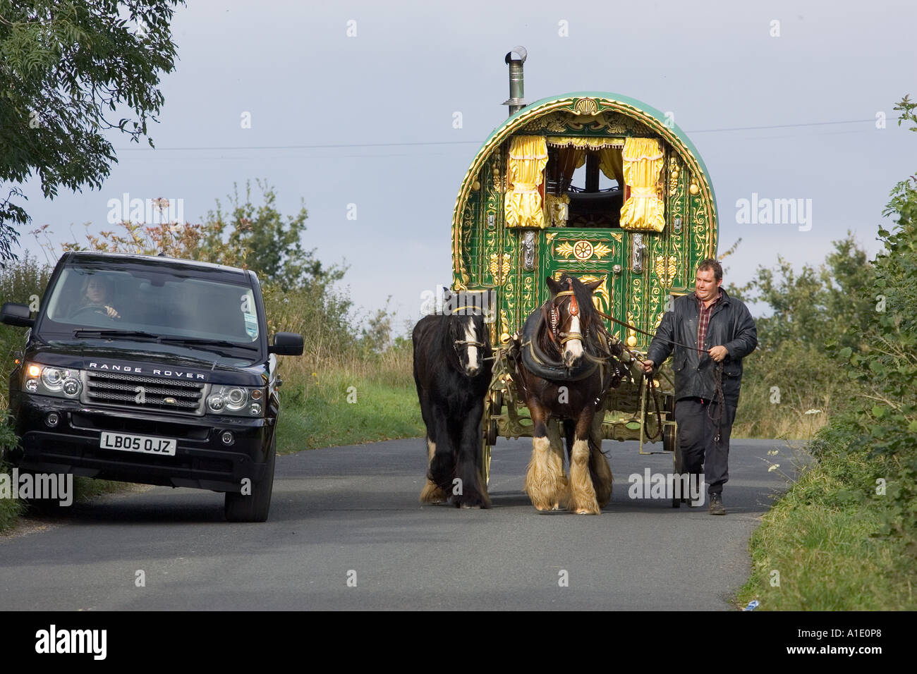 Range Rover car overtakes shire horse drawn gypsy caravan on country lane Stow On The Wold Gloucestershire United Kingdom Stock Photo