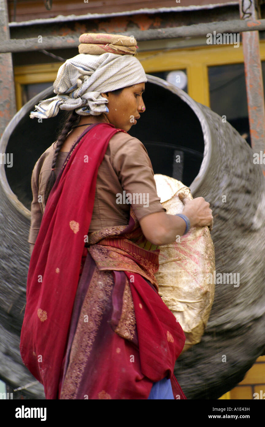 Young indian woman girl in red sari working hard manually at construction site filling agitator with gravel Stock Photo