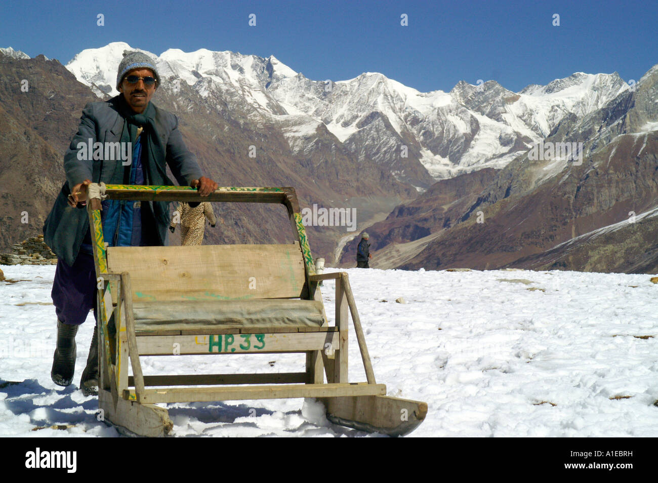 Indian man pushing empty wooden sleigh on snow in Indian Himalaya, Rohtang Pass in Lahaul region Stock Photo