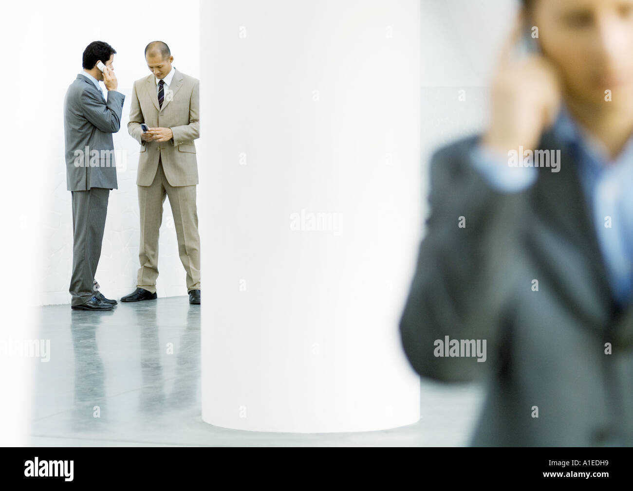 Businessmen in lobby using cell phones Stock Photo