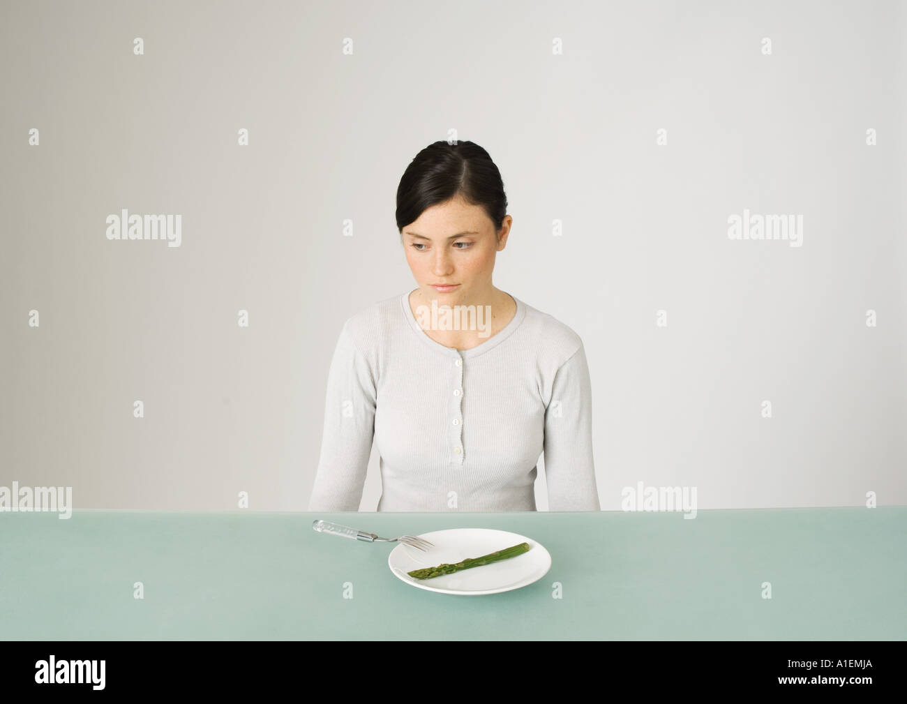 Young woman sitting in front of plate with single asparagus, looking away Stock Photo