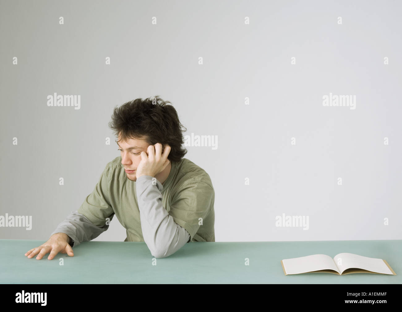 Young man talking on phone, turning away from open notebook on table Stock Photo