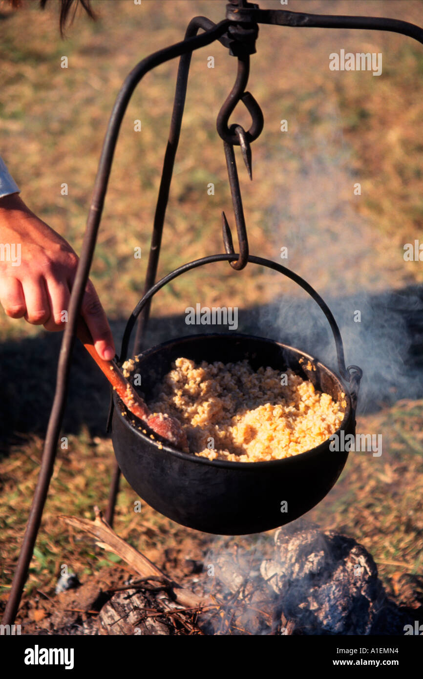 Suspended cast iron pot of cracked wheat porridge, cooking over an
