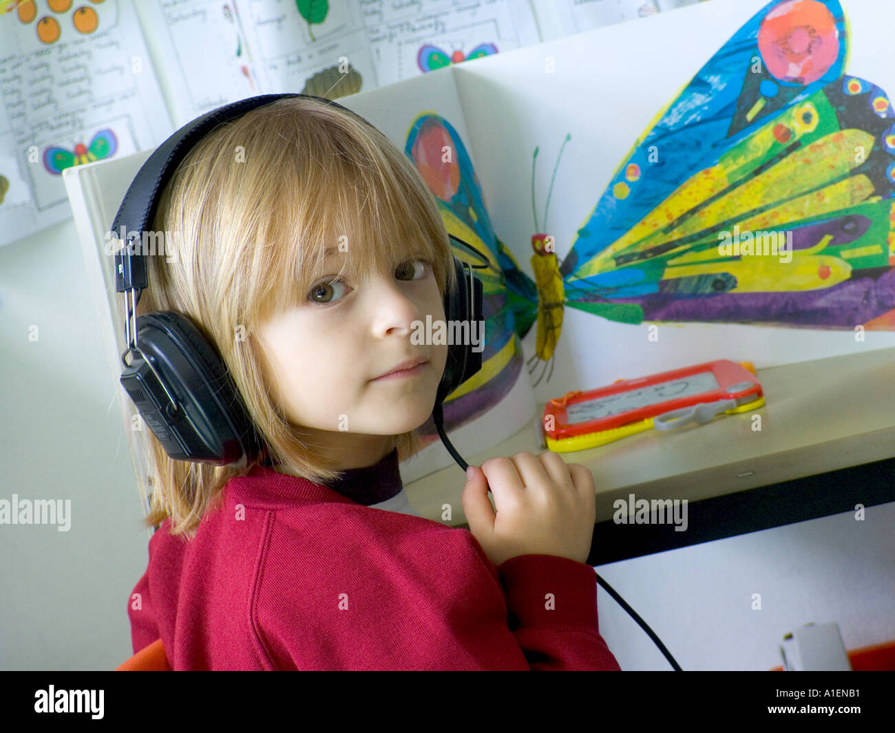 AUDIO EDUCATION Infant playschool child listens to an educational story through her headphones in school classroom Stock Photo