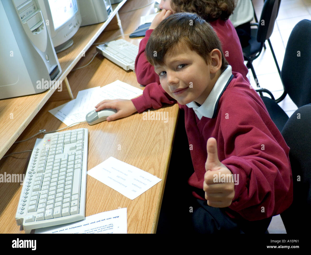 Confident junior schoolboy gives the thumbs up sign to camera in school computer classroom Stock Photo