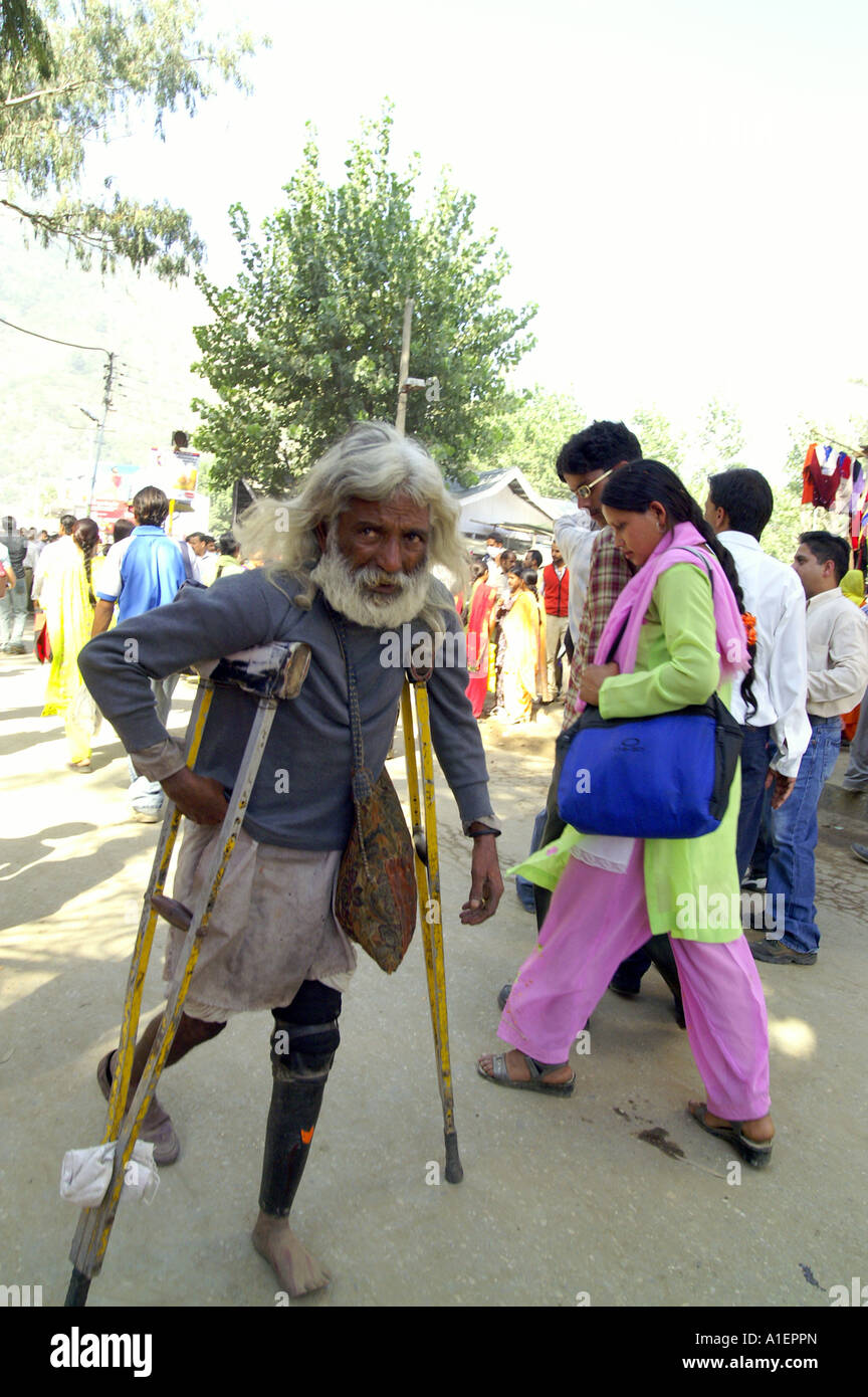 Old disabled indian man walking with support of crutch at Dussehra fair