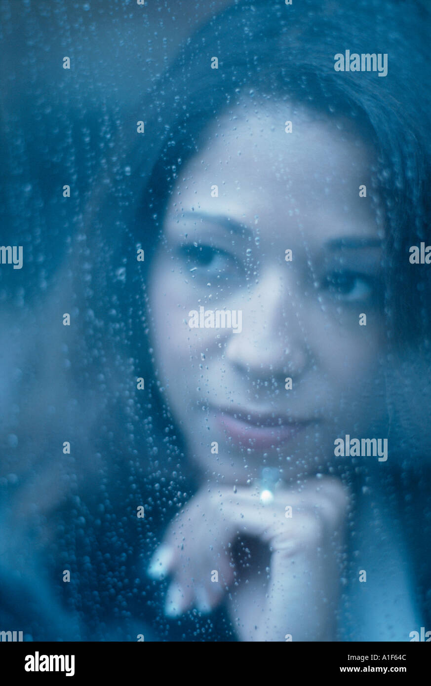 Moody portrait of African American woman looking through window on rainy day Stock Photo