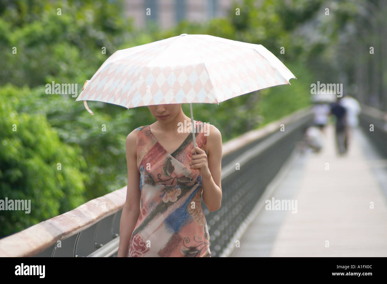 Chinese woman with umbrella walking across bridge in xujiahui park shanghai china and sheltering from the sun  Stock Photo