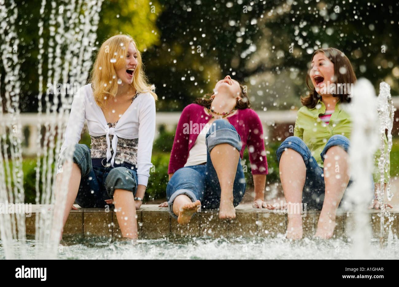 Three girlfriends have fun and laugh while cooling their feet in a fountain Stock Photo