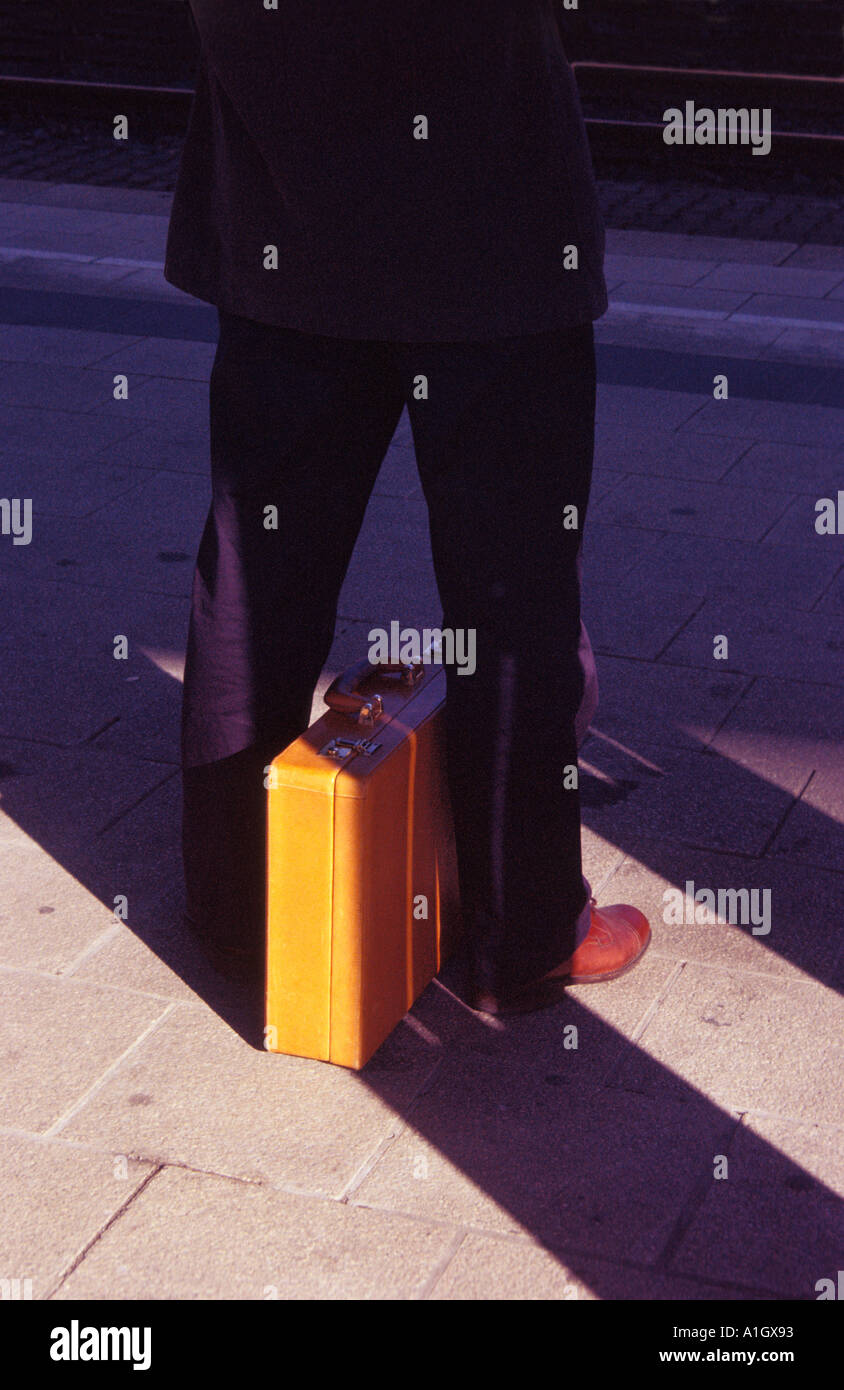 Business man with briefcase waits for a train at a railway station
