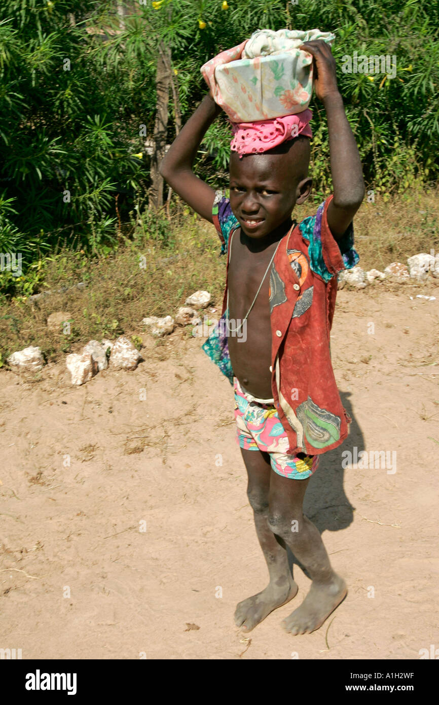 Small barefoot boy carries bowl on head Berending village south of The Gambia Stock Photo
