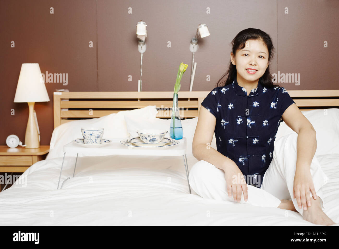 Portrait of a young woman sitting on the bed smiling Stock Photo - Alamy