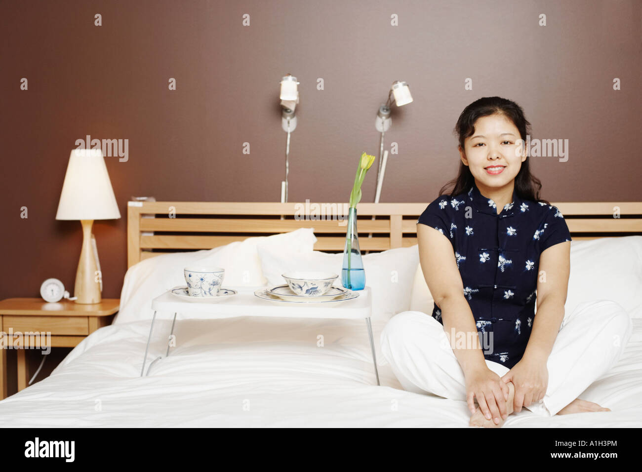 Portrait of a young woman sitting on the bed smiling Stock Photo - Alamy